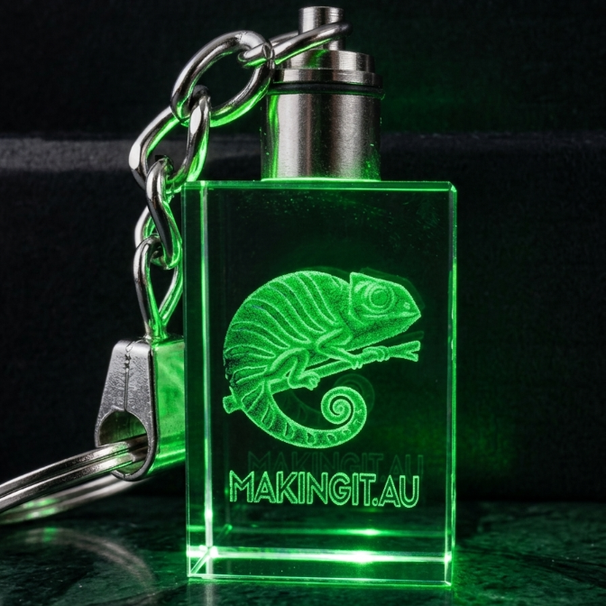 Keychain with a green LED light and chameleon design on a dark background