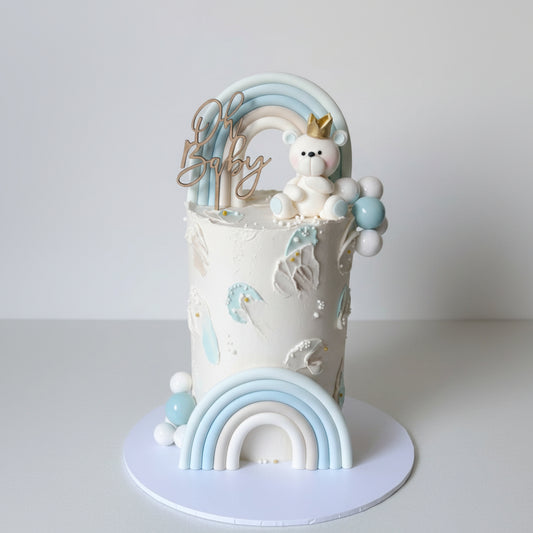 Baby shower cake with teddy bear, rainbow, and balloons on a white background
