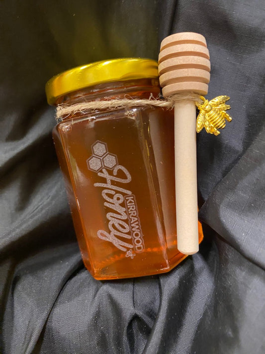 Jar of honey with a wooden dipper on a dark fabric background