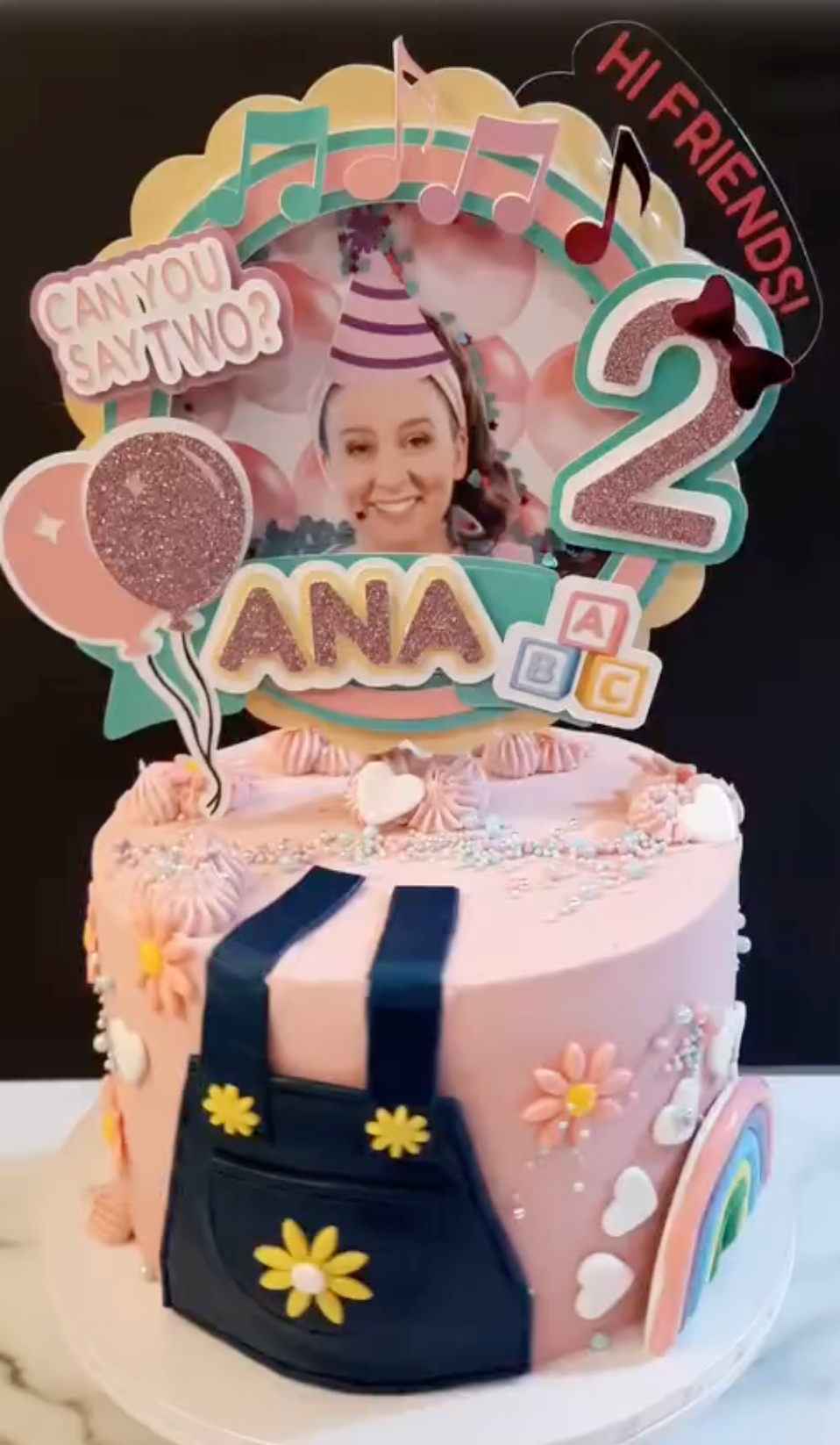 Birthday cake with decorative topper featuring a photo of a young girl, colorful text, and balloons.