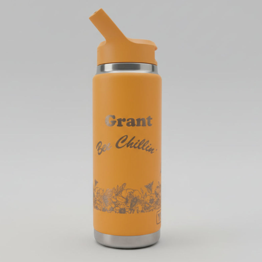 Orange waterbottle with a name and logo engraved on a white surface with a blurred background