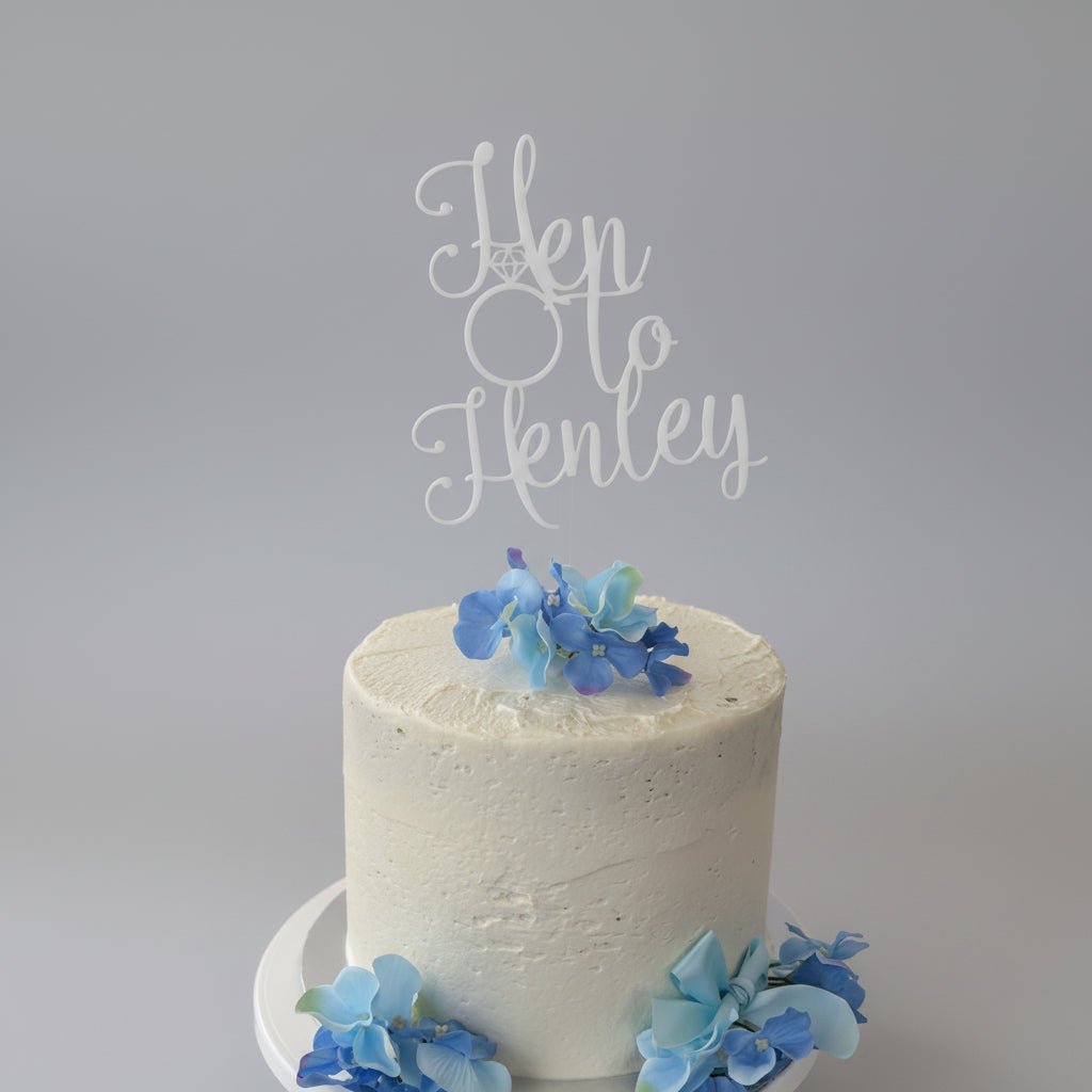 White cake with blue flowers and 'Hen to Henley' topper