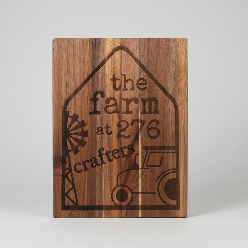 Wooden cutting board with engraved text 'the farm at 276 crafters' on a wooden surface.