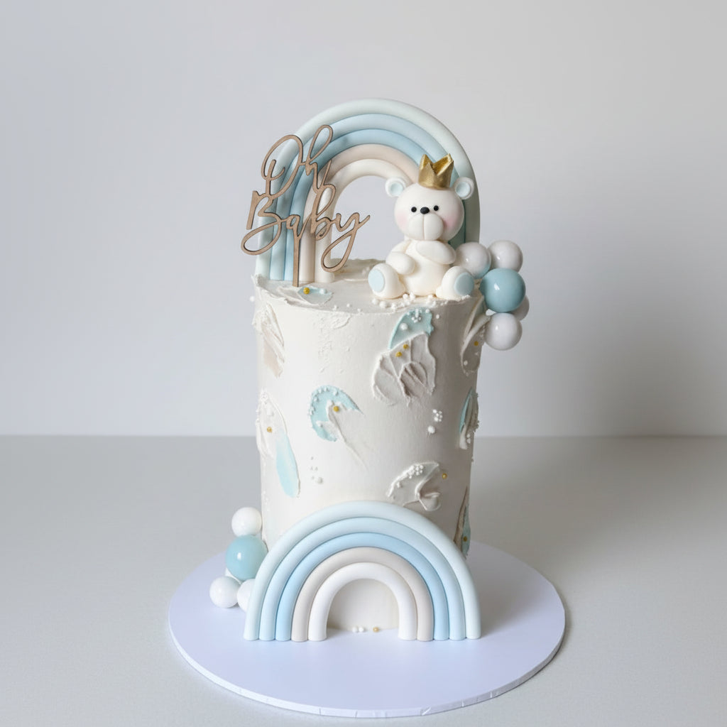 Baby shower cake with teddy bear, rainbow, and balloons on a white background