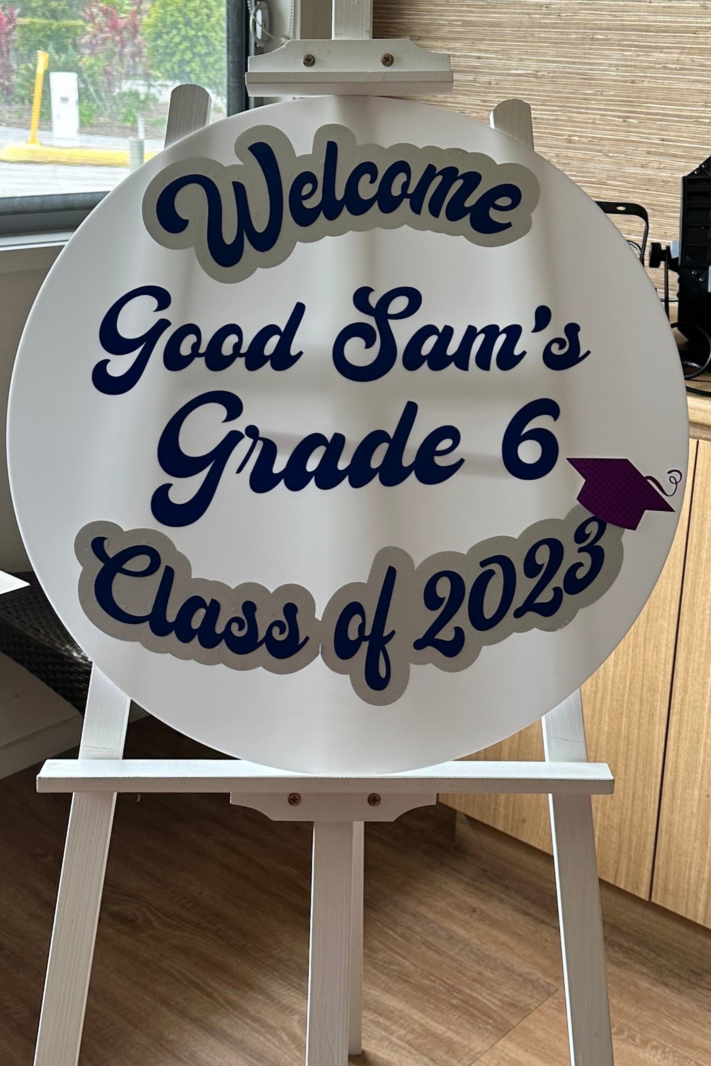 Decorative sign for Good Sam's Grade 6 Class of 2023 on an easel stand indoors.